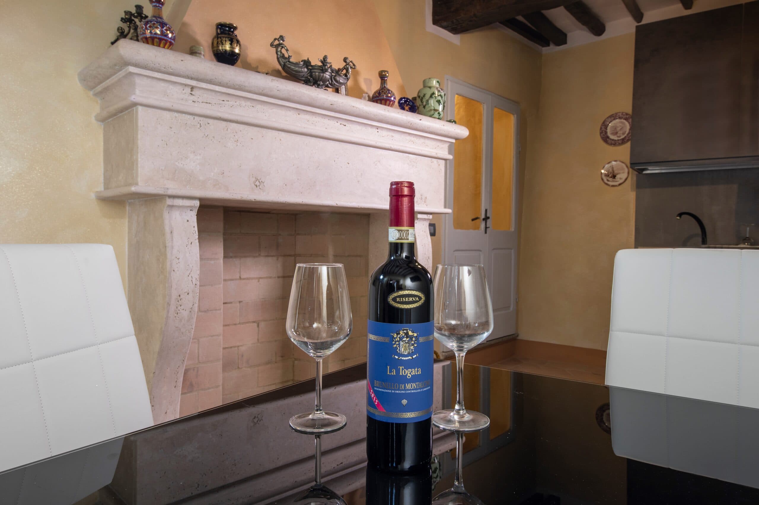 La sala condivisa del Relais Il Terrazzo, con camino, tavolo da pranzo e una bottiglia La Togata