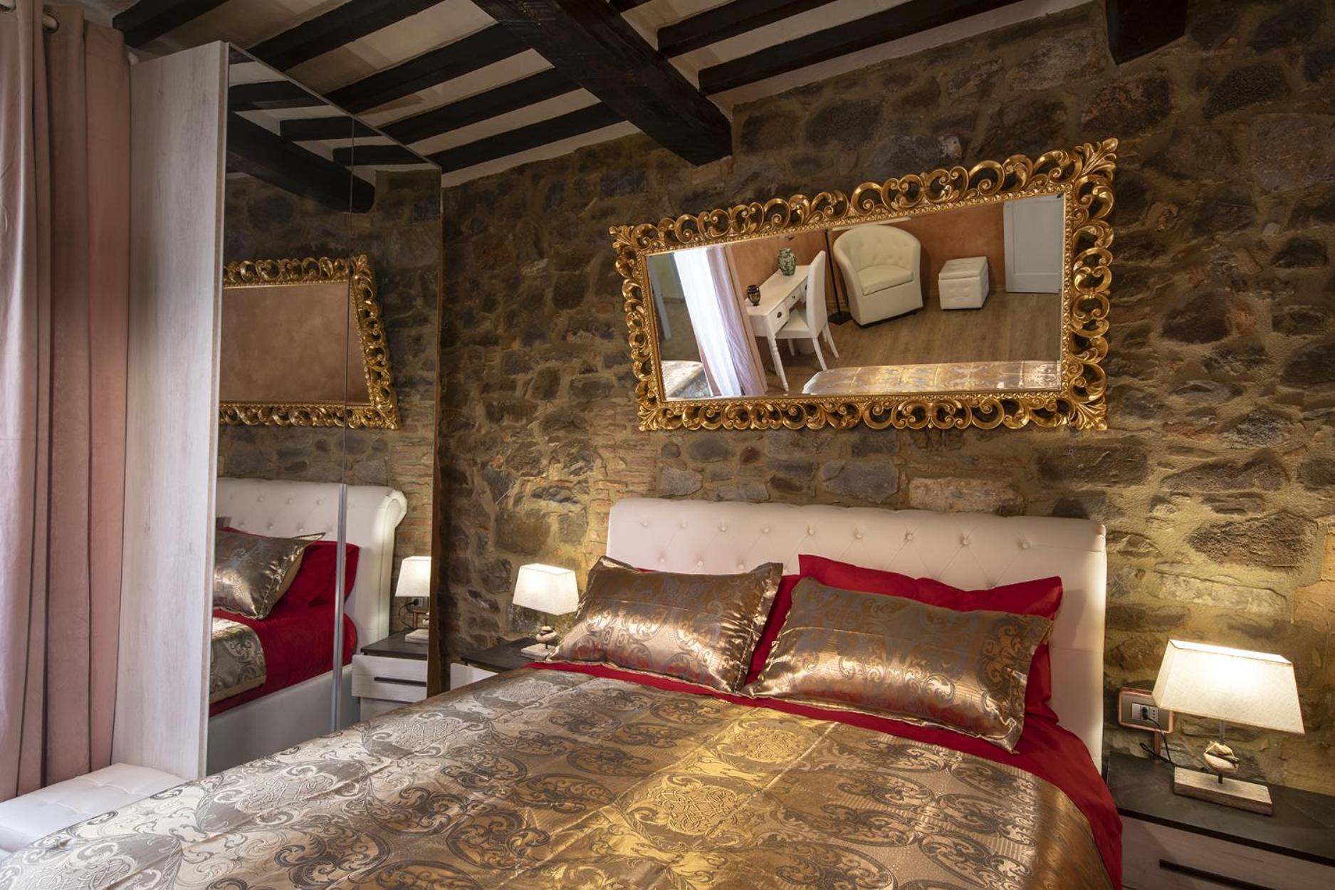 Matrimoniale Deluxe di Cleopatra: the bed against an exposed-stone wall, with gilded mirrors and chestnut beams