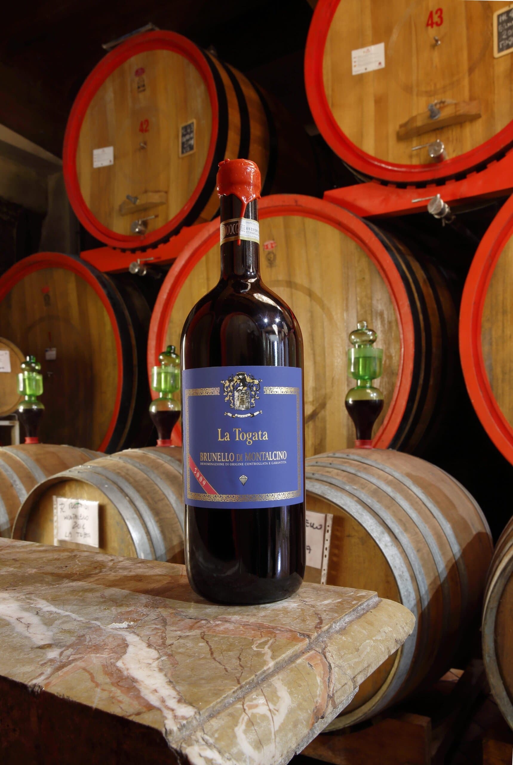 Una bottiglia di Brunello di Montalcino de La Togata davanti alle botti della cantina